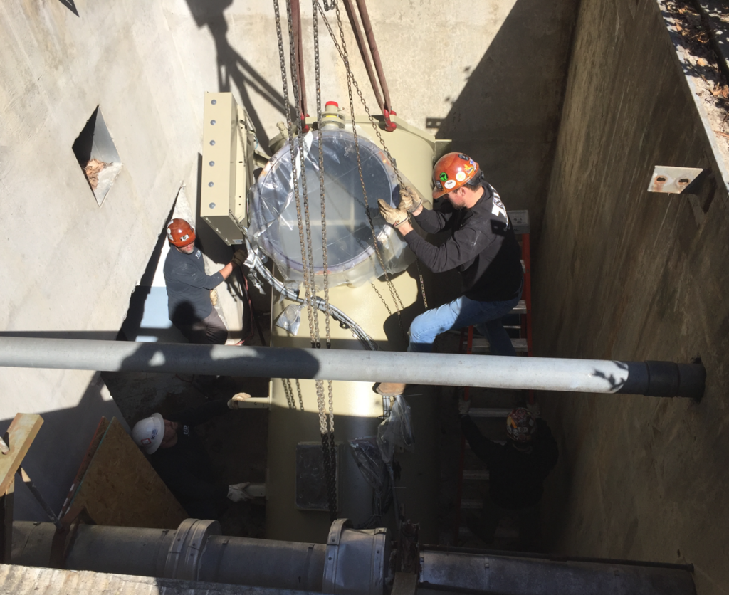 workers guide a chiller part as it it lifted into place